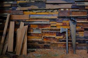 El hacha con mango de metal y la sierra de mano apoyada contra las paredes viejas están hechas de diferentes tipos de madera foto