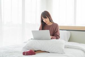 Mujer asiática que trabaja con el portátil en la cama en casa foto