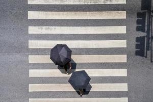 Vista superior de la foto aérea de la gente bajo el paraguas caminar en la calle de la ciudad sobre el tráfico de paso de peatones