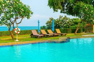Piscina de sillas o camas y sombrillas alrededor de la piscina con fondo de mar - vacaciones y concepto de vacaciones