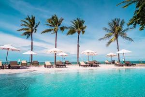 Chair pools or beds and umbrellas around swimming pool with sea background - Holidays and vacation concept