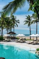 Chair pools or beds and umbrellas around swimming pool with sea background - Holidays and vacation concept photo