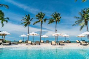 Piscina de sillas o camas y sombrillas alrededor de la piscina con fondo de mar - vacaciones y concepto de vacaciones foto