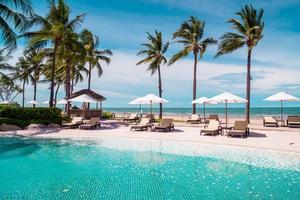 Chair pools or beds and umbrellas around swimming pool with sea background - Holidays and vacation concept photo