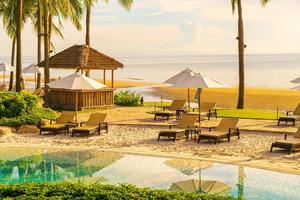 Hermosas sombrillas y sillas de lujo alrededor de una piscina al aire libre en un hotel y resort con palmeras de coco en el cielo al atardecer o al amanecer - concepto de vacaciones y vacaciones