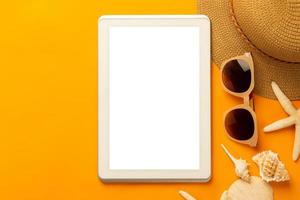 Summer background with blank screen tablet and beach accessories, mask to prevent covid-19 on vibrant orange background top view with copy space. photo