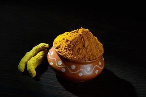 Turmeric powder in clay pot with roots or barks on black background photo