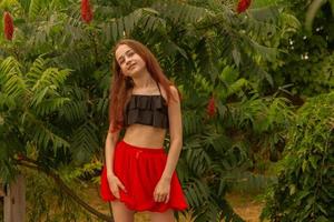 Teenage girl on a background of greenery. A young girl in a red skirt in the summer. photo