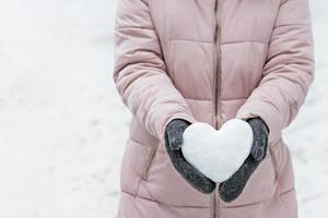 manos de mujeres en guantes grises cálidos con un corazón blanco como la nieve. el concepto del dia de san valentin foto