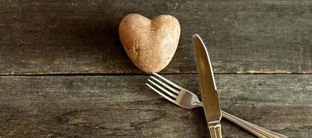 Red potatoes in the shape of a heart on a wooden background with a fork and knife. The concept of agriculture, harvesting, vegetarianism. Valentine's Day. square, ugly food.