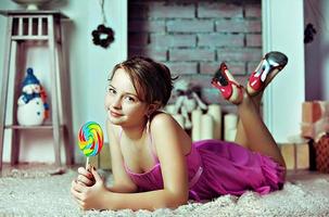 A young girl with a candy on a stick in her hands in a pink dress on the background of Christmas decorations photo