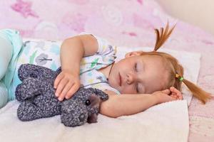 una niña pequeña está durmiendo en una cama con juguetes abrazados. infancia. foto