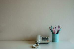 Teléfono y lápices de colores pastel en el cristal azul sobre el escritorio en el fondo de la pared gris foto