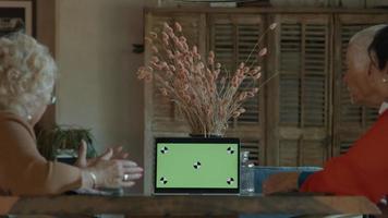 Zwei Frauen, ein Mann und ein Mädchen am Tisch mit Videoanruf auf Laptop mit grünem Bildschirm green