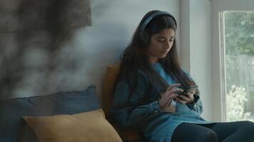 Girl with headphone sitting in corner whilst typing on smartphone video