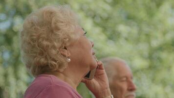 Woman talks on phone whilst laughing and sitting next to man in garden video