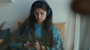 Girl with headphone sitting in corner whilst typing on smartphone video