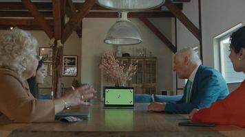 Dos mujeres, un hombre y una niña en la mesa con videollamadas en un portátil con pantalla verde video