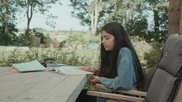 Girl sitting at table in garden doing homework reading aloud video