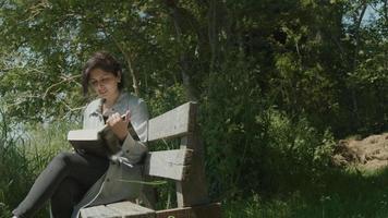 mulher sentada em um banco de madeira no campo lendo um livro video