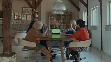 Zwei Frauen, ein Mann und ein Mädchen am Tisch mit Videoanruf auf Laptop mit grünem Bildschirm green