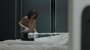 Mujer plancha la camisa en el dormitorio y ajusta el cable eléctrico video