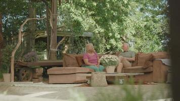 kvinna och man som sitter på soffan i trädgården som har en livlig konversation video
