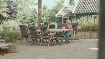 två kvinnor som har konversation som sitter vid bordet i trädgården video