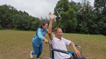 gelukkig lachend grootvader in rolstoel ontspannen met zijn armen omhoog genietend van de natuur met kleindochter op een zonnige dag in het park. gezinsleven op vakantie.