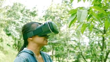 glückliche Frau, die eine VR-Headset-Brille der virtuellen Realität im Wald trägt und die Natur an einem sonnigen Sommertag im Frühlingsgarten genießt. modernes Technologiekonzept. video