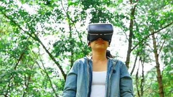 Happy woman wearing VR-headset glasses of virtual reality in forest and enjoying the nature on a sunny summer day in spring garden. Modern technology concept. video