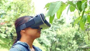 Happy woman wearing VR-headset glasses of virtual reality in forest and enjoying the nature on a sunny summer day in spring garden. Modern technology concept. video