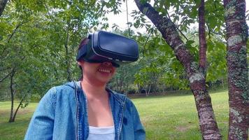 Happy woman wearing VR-headset glasses of virtual reality in forest and enjoying the nature on a sunny summer day in spring garden. Modern technology concept. video