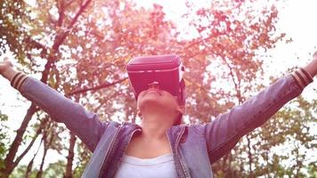 glückliche Frau, die eine VR-Headset-Brille der virtuellen Realität im Wald trägt und die Natur an einem sonnigen Sommertag im Frühlingsgarten genießt. modernes Technologiekonzept. video