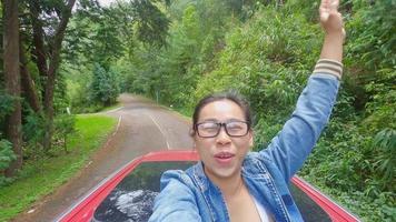 Cheerful woman spread arms on car rooftop under bright sky at mountain with nature background during road trip on vacation. video