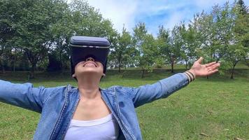 Happy woman wearing VR-headset glasses of virtual reality in forest and enjoying the nature on a sunny summer day in spring garden. Modern technology concept.
