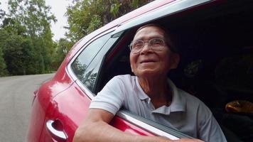 gelukkige senior man opent het raam om het prachtige uitzicht op de auto te zien genieten van een natuur road trip met familie. lachende grootvader met hoofd en hand uit autoraam genieten van uitzicht. video