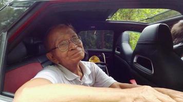 Happy senior man opens the window to see the beautiful view on the car enjoying a nature road trip with family. Smiling grandfather with head and hand out of car window enjoying view. video