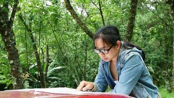 mulher viajando de carro, fazendo uma pausa para olhar um mapa durante uma viagem no parque nacional. turista feminina encostado no capô de um carro, procurando instruções no mapa. video