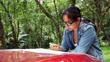 donna che viaggia in auto prendendo una pausa per guardare una mappa durante un viaggio nel parco nazionale. turista femminile appoggiato a un cofano anteriore dell'auto in cerca di indicazioni sulla mappa. video