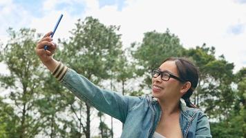 una turista feliz hablando de una videollamada en su teléfono inteligente con sus amigos en unas vacaciones de verano en un parque de primavera. concepto de viaje y felicidad. video