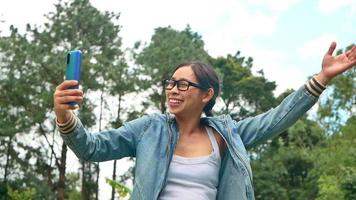 Retrato de una mujer con gafas mirando a la cámara con cara sonriente de pie en medio de la naturaleza en el jardín de primavera. conceptos de viaje y felicidad. video