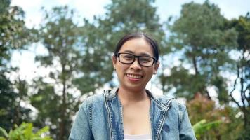 Portrait of a woman in glasses looking at the camera with smiley face standing in the midst of nature in the spring garden. Travel and happiness concepts. video