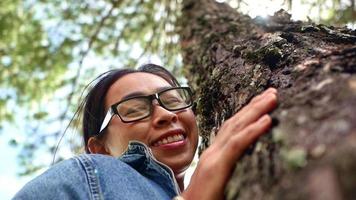 en glad kvinna står nära majestätiska träd och kramar med kärlek en solig sommardag i parken. jorddag och icke-avskogning koncept. video
