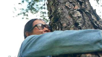 una mujer feliz está de pie cerca de un árbol majestuoso y se abraza con amor en un día soleado de verano en el parque. día de la tierra y concepto de no deforestación.