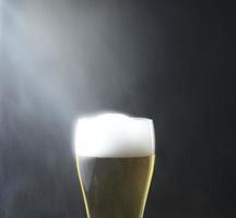 A glass of foamy cold beer with smoke aerosol, water dust spalshing over, aginst black dark background. Front view shot. Center, vertical or square, epic image style. photo