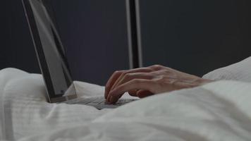 Los dedos del hombre escribiendo en el portátil en la cama