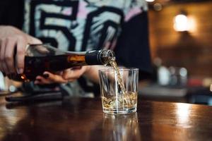 whiskey is poured into a glass from a bottle photo