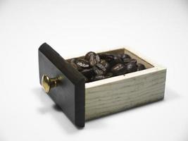 Granos de café en la pequeña caja de madera del molinillo de café sobre fondo blanco. de cerca foto
