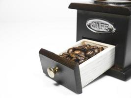 Granos de café en una pequeña caja de molinillo de café de madera sobre fondo blanco. foto